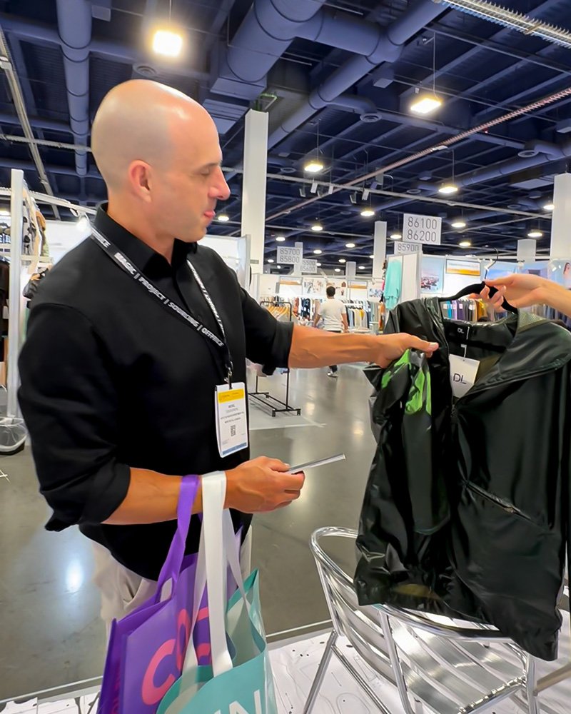 Buyer inspecting thermochromic color-changing hoodie at DOLUXE MAGIC Show booth