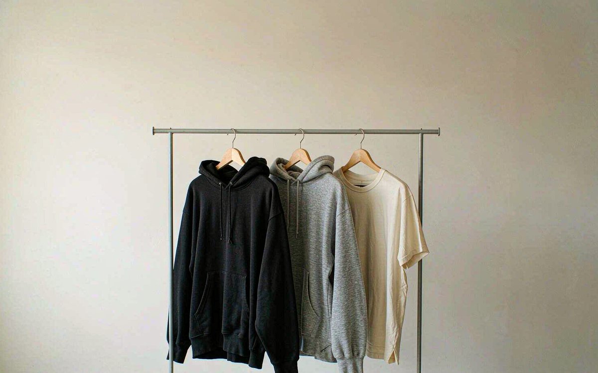 A minimal capsule collection of three heavyweight garments on a clothing rail against a clean wall